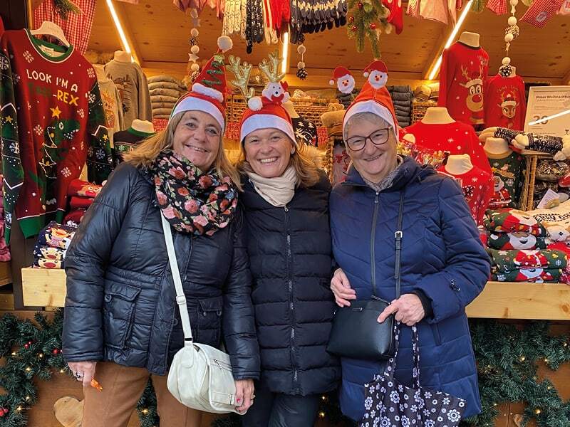 Trois voyageuses coiffées de bonnets de Père Noël devant un stand du marché d’Ulm