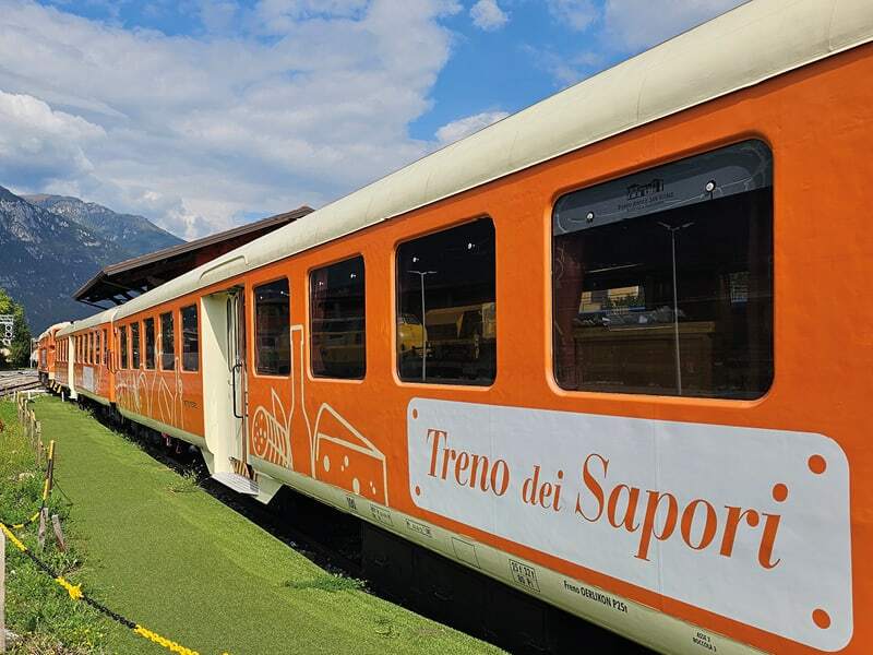 Wagons orange du train des saveurs Treno dei Sapori devant les montagnes