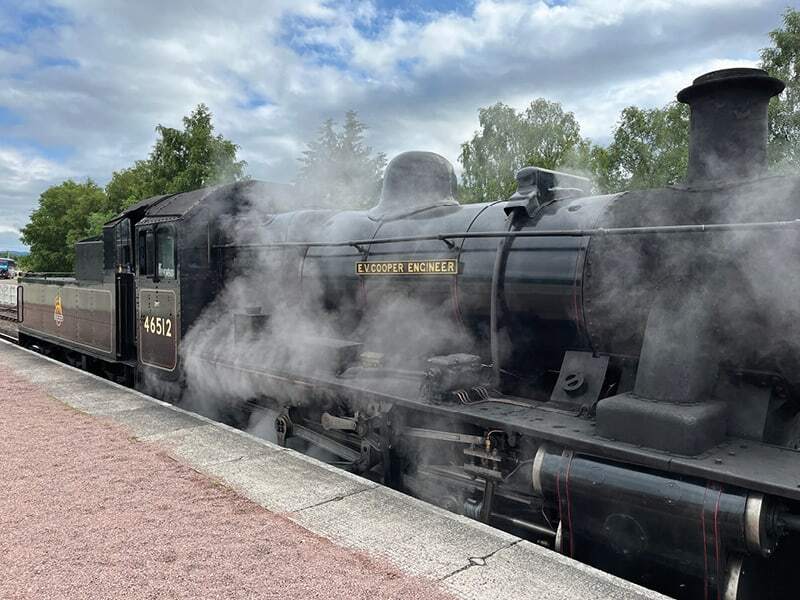 Locomotive à vapeur noire enveloppée de fumée le long d’un quai de gare