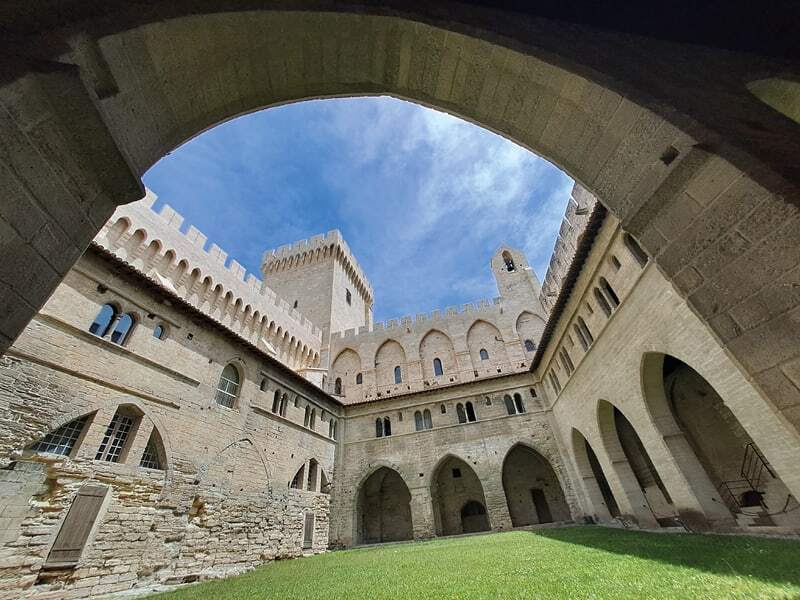 Cour du palais des Papes d’Avignon vue depuis une arcade sous un ciel bleu