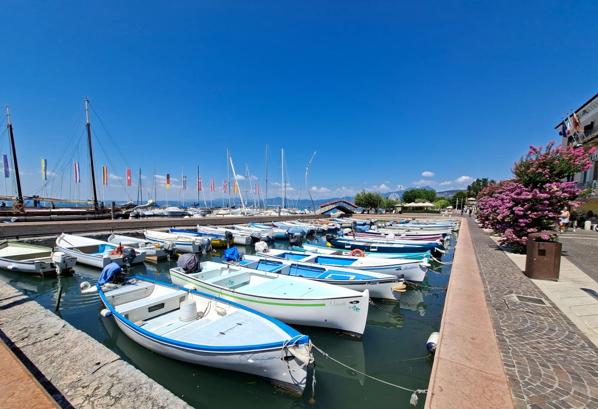 Hafenpromenade am Gardasee mit zahlreichen kleinen Booten und blauem Himmel.