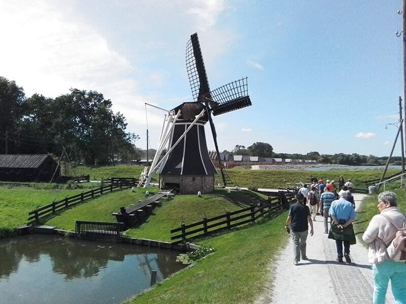 Moulin à vent au bord d’un étang et groupe de visiteurs sur un chemin ensoleillé