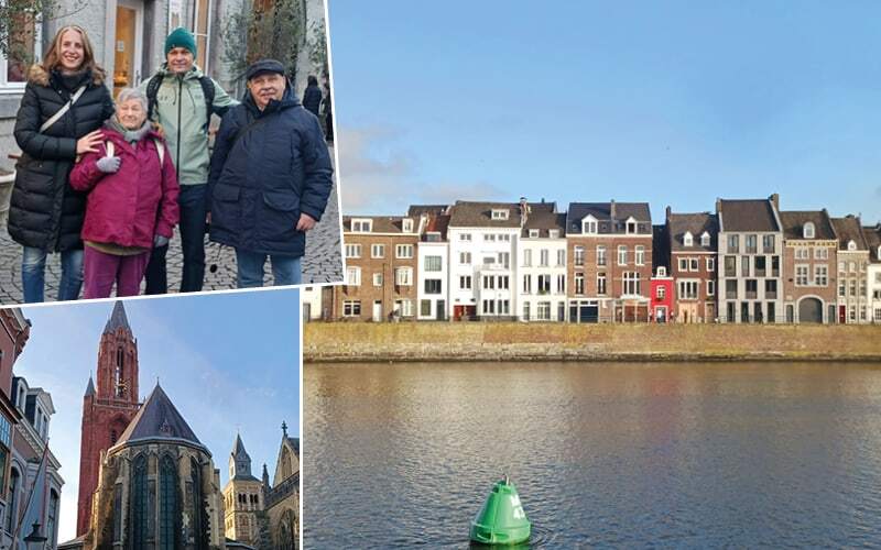 Voyageurs en ville, église gothique à tour rouge et maisons alignées au bord de la Meuse