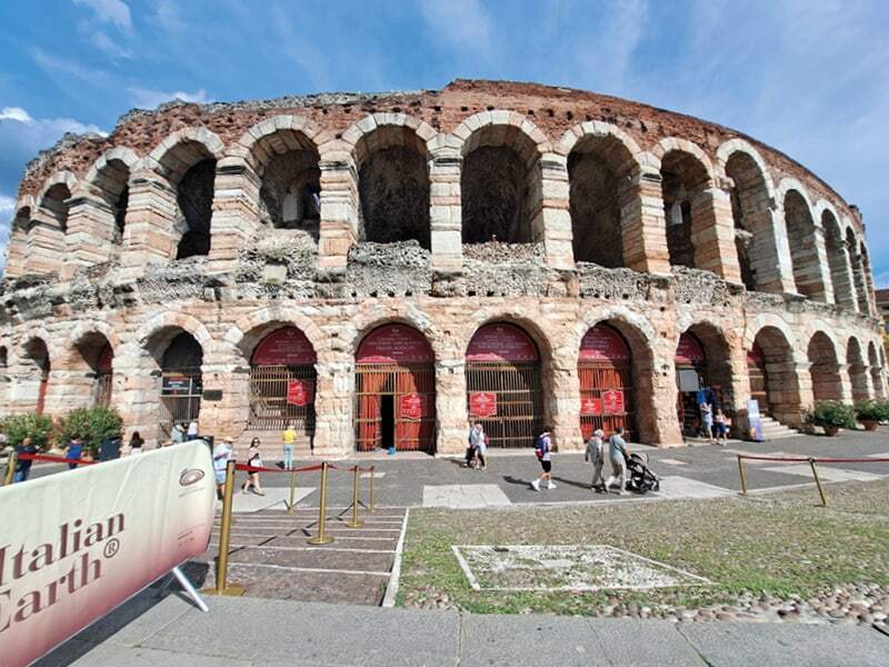 Arènes romaines de Vérone sous un ciel bleu, avec quelques passants devant les arcades