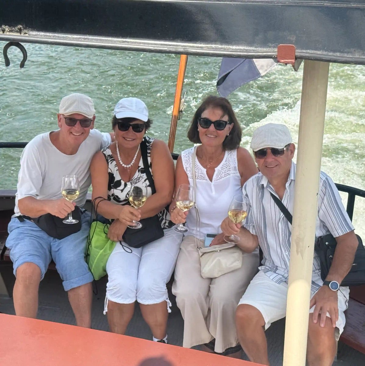 Vier gut gelaunte Reiseteilnehmer geniessen bei einer Bootsfahrt gemeinsam ein Glas Wein.