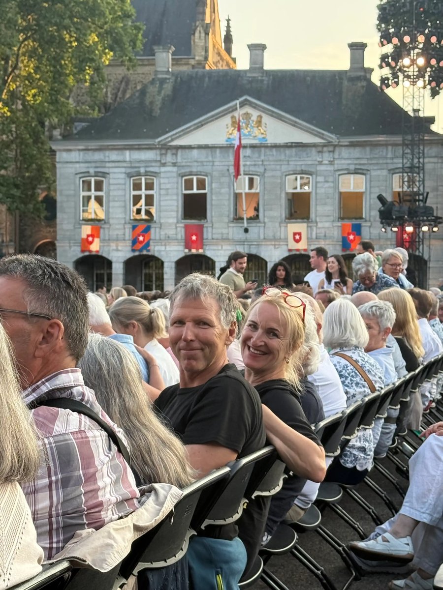 Zwei gut gelaunte Reiseteilnehmer sitzen inmitten des Publikums bei einem Open-Air-Konzert.