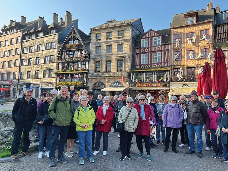 Groupe de voyageurs souriants devant les maisons à colombages de la place du Vieux-Marché à Rouen