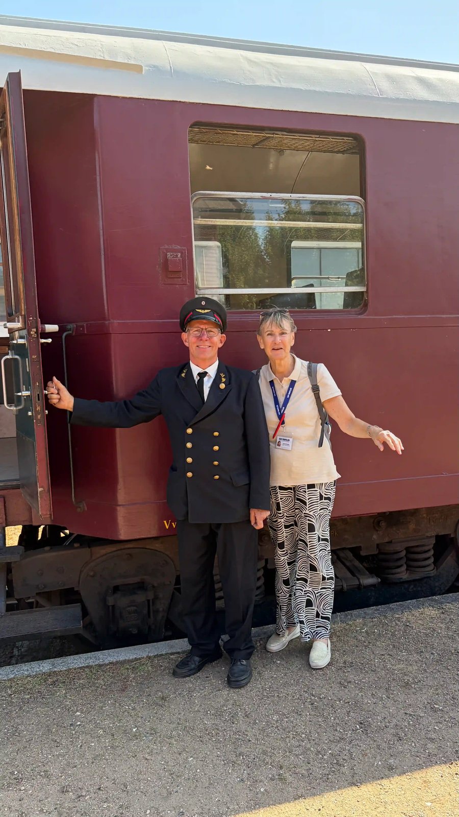 Reiseleiterin mit Zugbegleiter vor einem historischen Eisenbahnwagen.