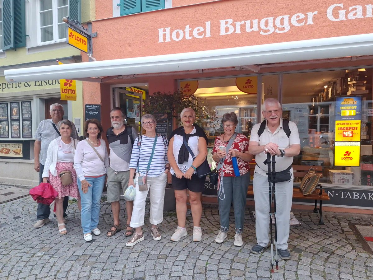 Groupe de huit voyageurs posant devant une façade rose avec l'enseigne Hotel Brugger