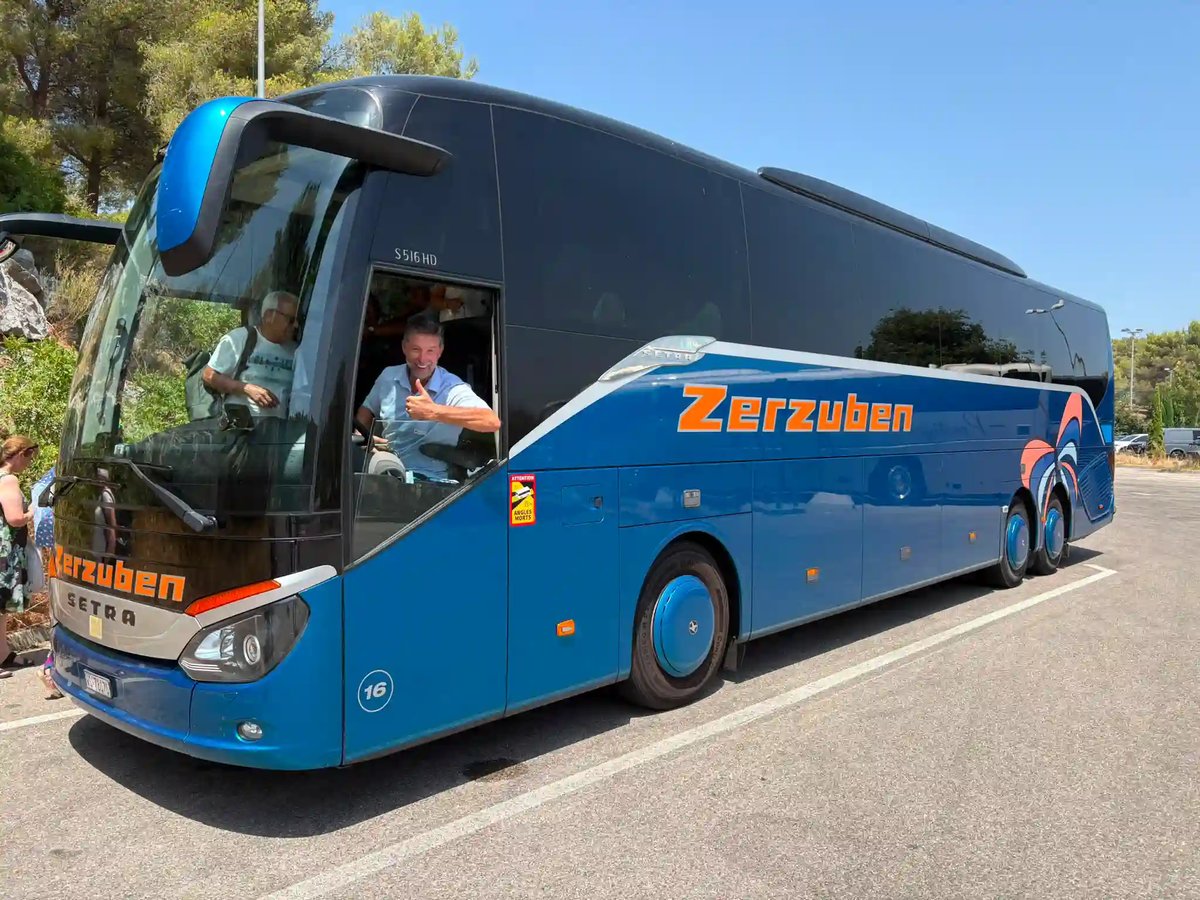 Blauer Reisecar von Zerzuben mit lächelndem Chauffeur an einem sonnigen Reisetag.