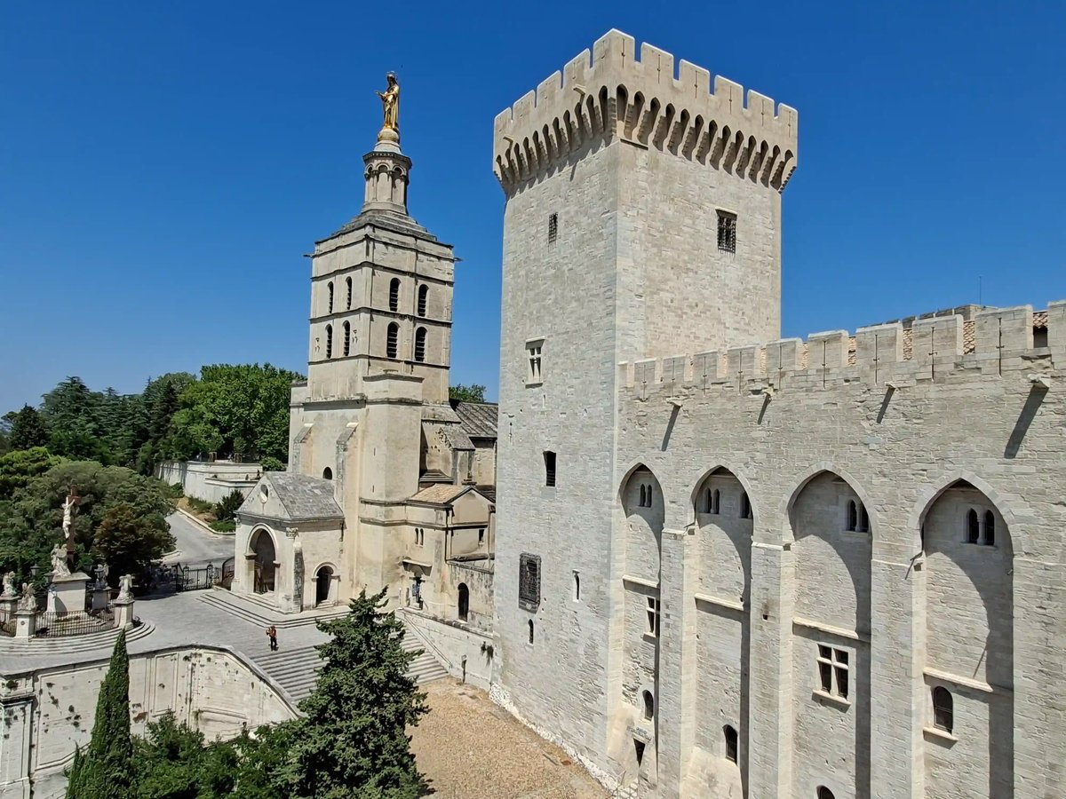 Papstpalast und Kathedrale Notre-Dame-des-Doms in Avignon unter blauem Himmel.