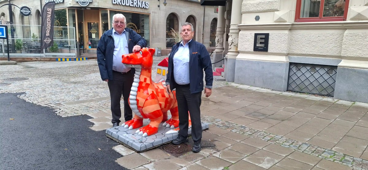 Zwei Chauffeure stehen neben einer roten Drachenfigur in einer Stadt