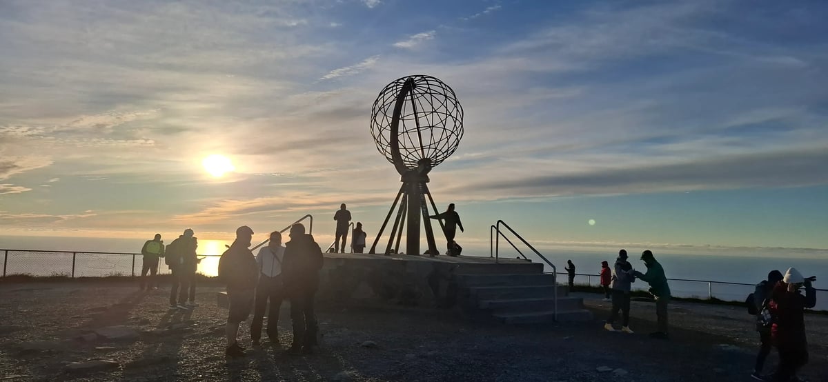 Nordkapkugel und Besucher im Licht der tief stehenden Mitternachtssonne