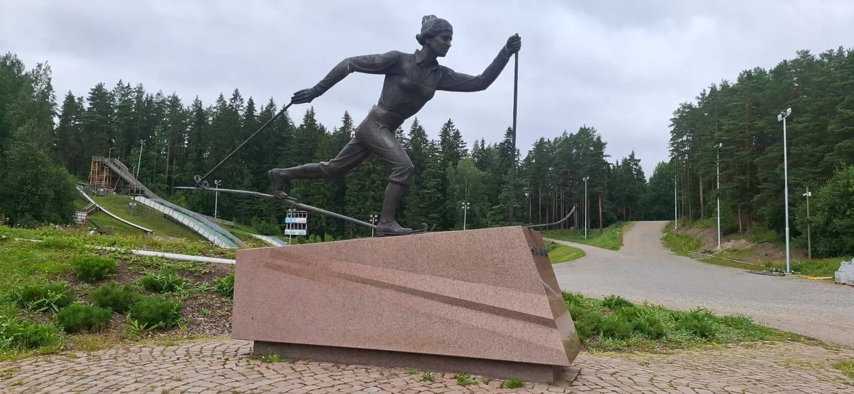 Bronzestatue einer Skilangläuferin vor einer Skisprungschanze in Lahti