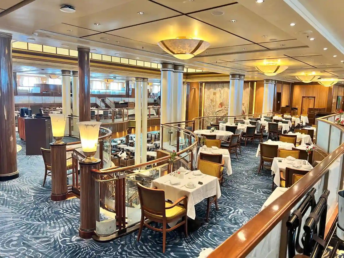 Eleganter Speisesaal der Queen Mary 2 mit gedeckten Tischen, Säulen und geschwungener Balustrade