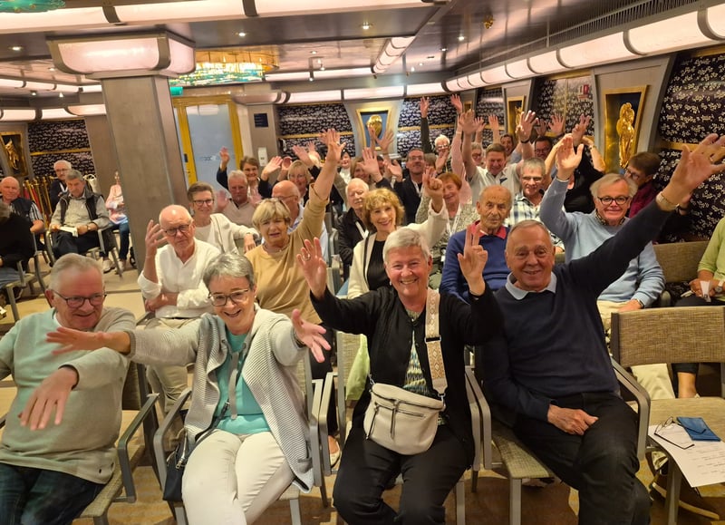 Gut gelaunte Reisegruppe an Bord der Costa Favolosa mit erhobenen Händen.