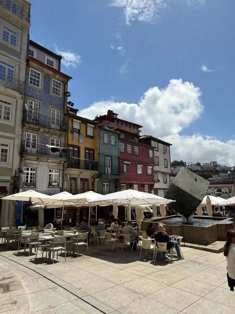 Sonniger Platz mit bunten Häusern, Strassencafés und Brunnen.