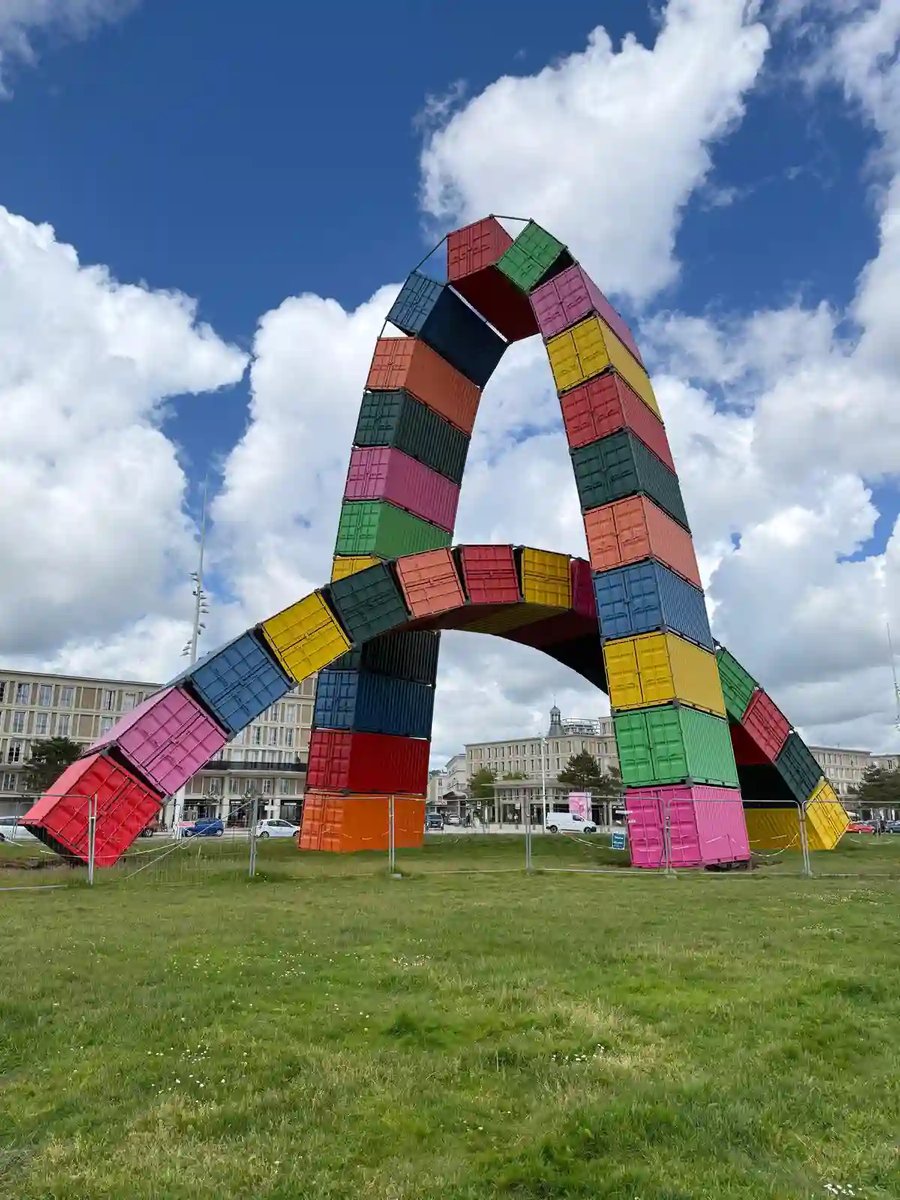 Grosses Kunstwerk aus bunten Schiffscontainern unter blauem Himmel.