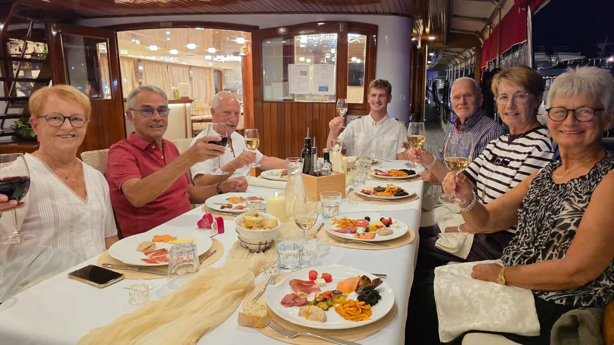 Le capitaine et six voyageurs trinquent autour d’une table dressée sur le pont du yacht Barbara