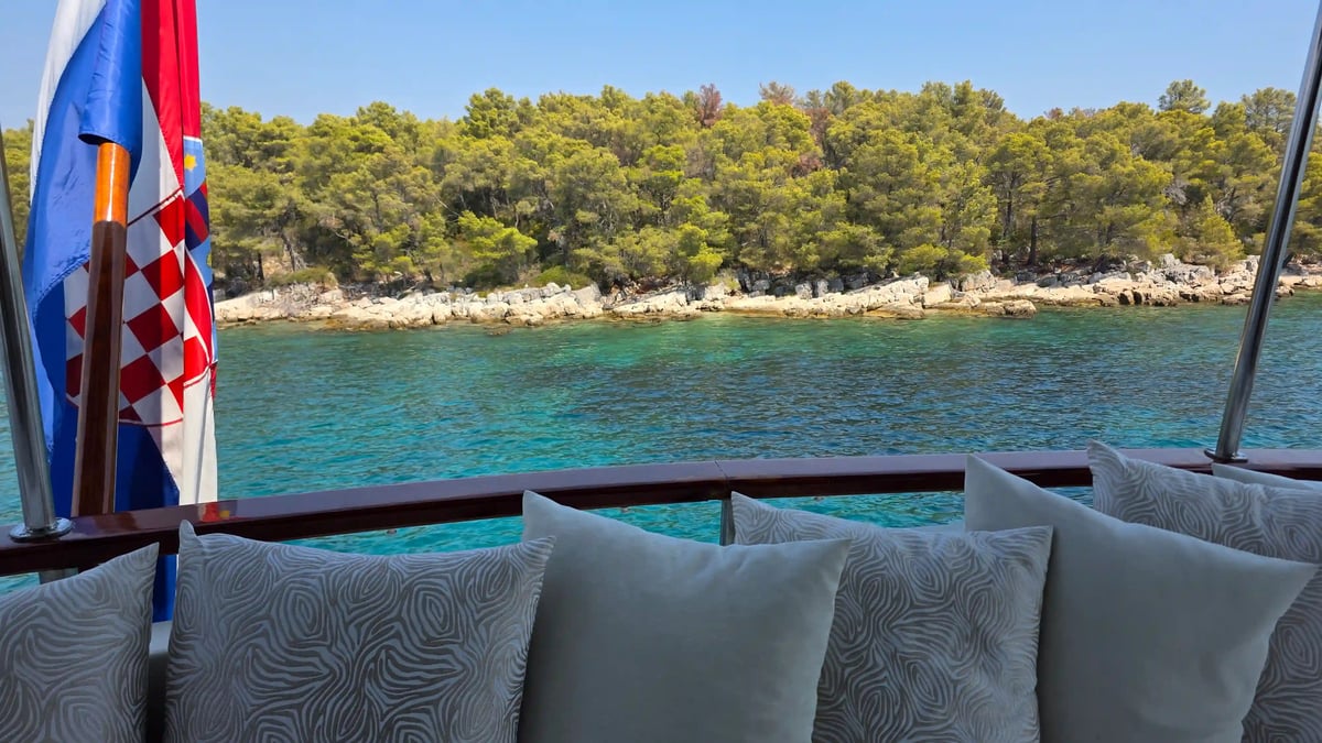 Espace détente du yacht Barbara avec coussins, face aux eaux turquoise et à la côte verdoyante