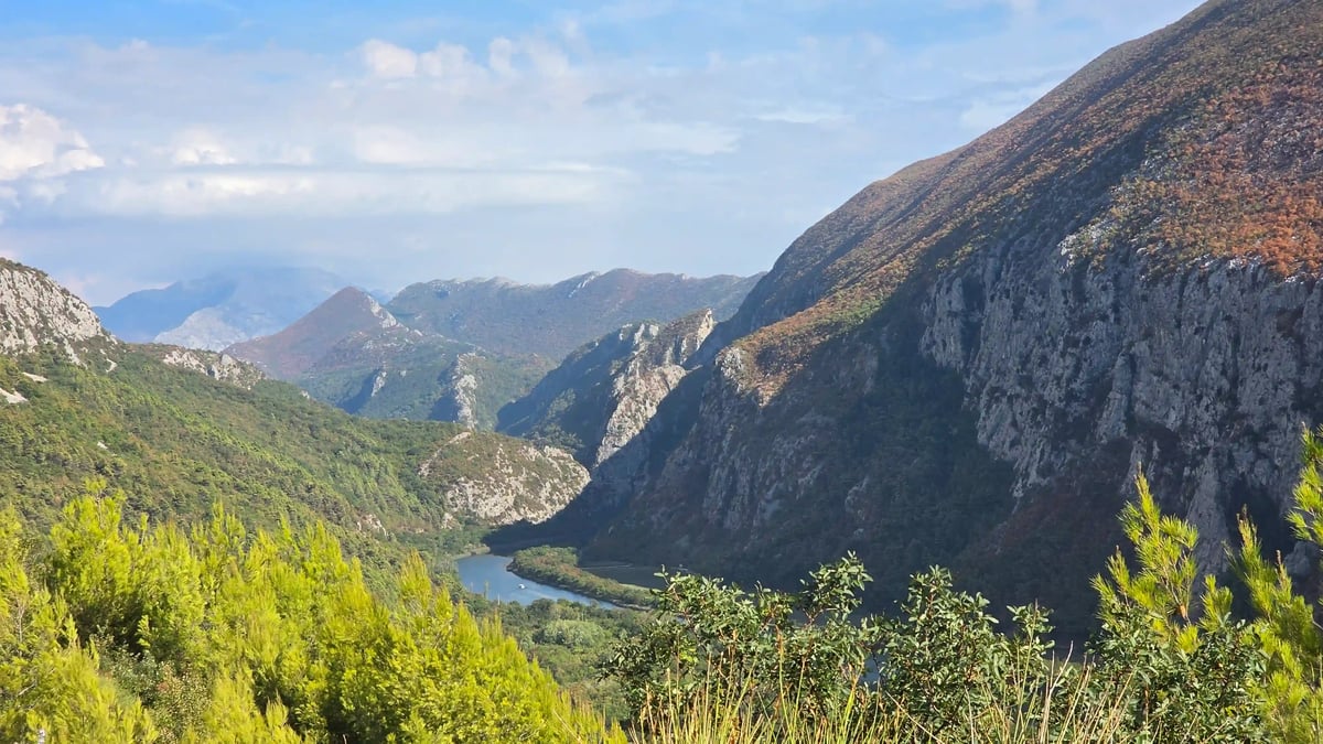 Paysage montagneux verdoyant traversé par une vallée profonde sous un ciel bleu
