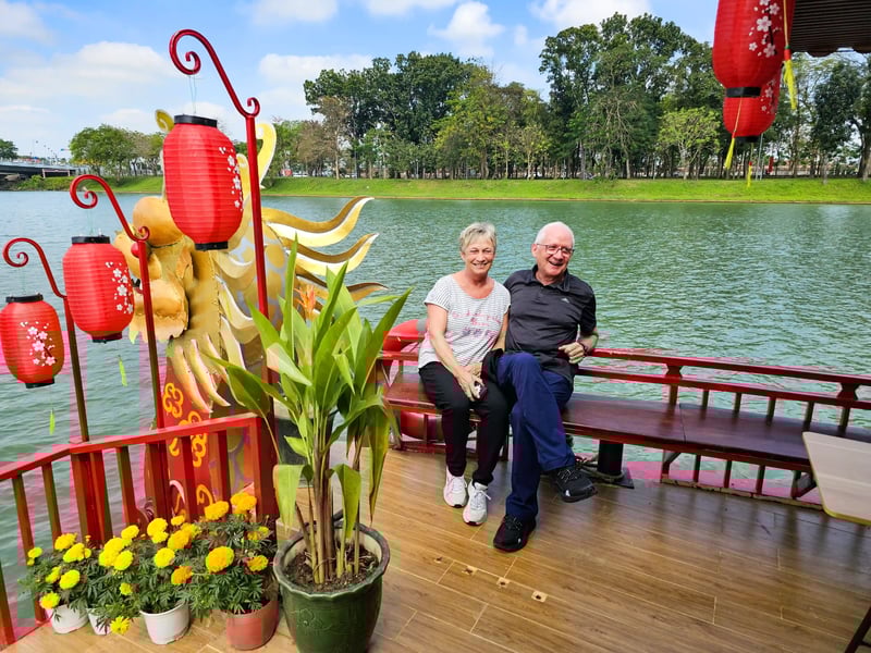 Ein älteres Ehepaar sitzt lächelnd auf einer Bank auf einem dekorierten Holzboot.
