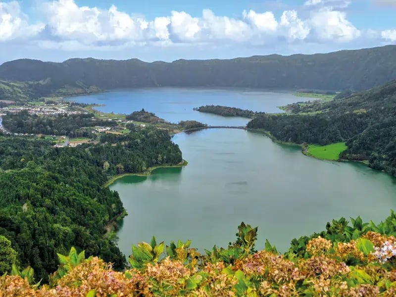 Aussicht auf zwei verbundene Seen mit grünen Hügeln, Wald und Wolken am Himmel