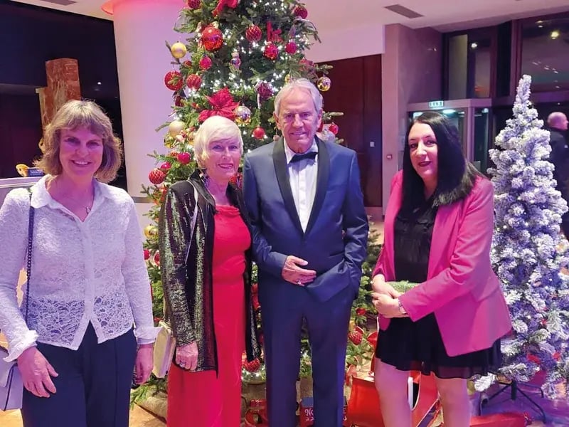 Vier Personen in festlicher Kleidung vor geschmücktem Weihnachtsbaum in Innenraum