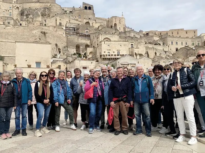 Reisegruppe steht vor einer historischen Felsenstadt mit dicht gebauten Häusern