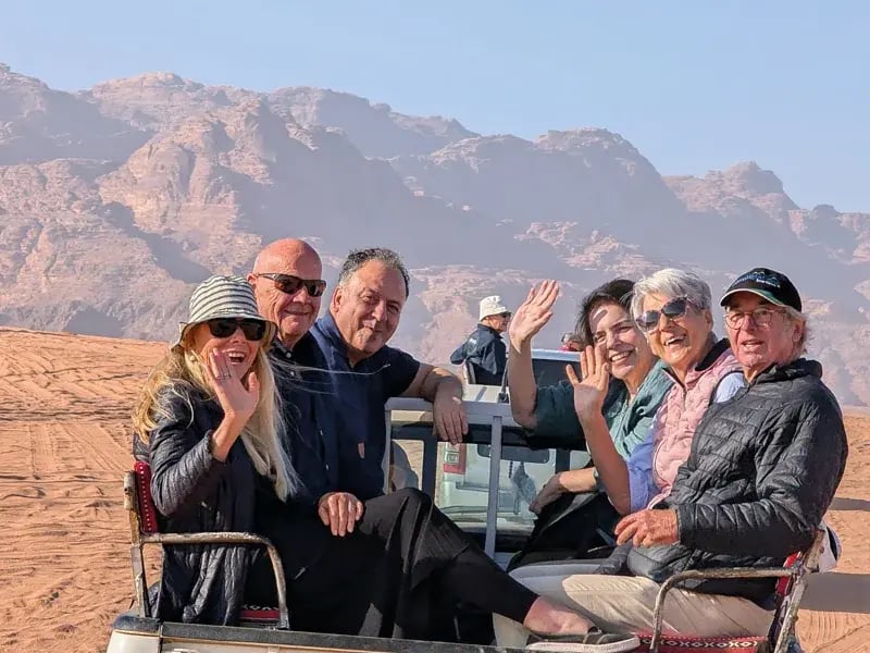 Gruppe von Personen in einem offenen Fahrzeug in einer Wüste mit Felsen im Hintergrund