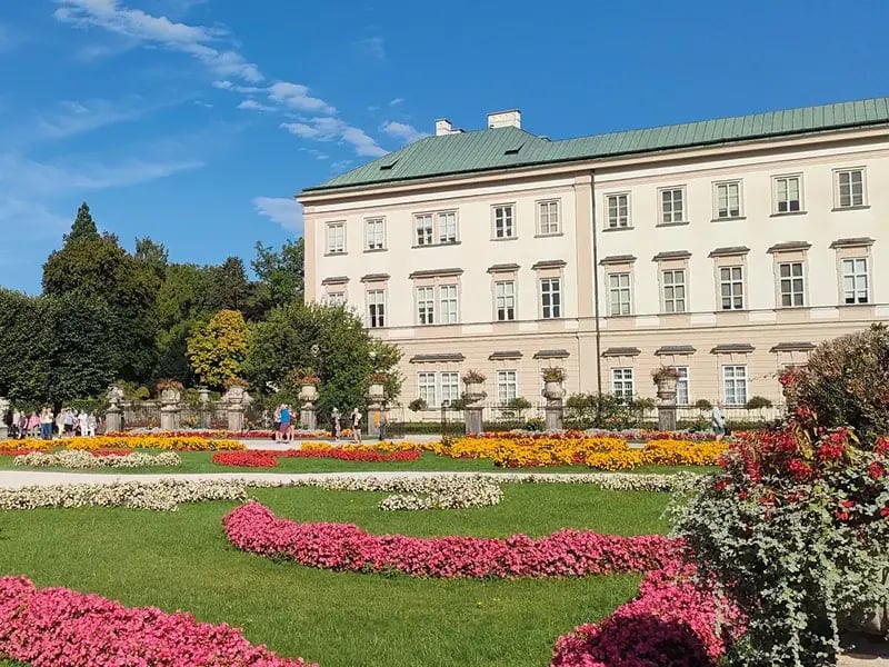 Schlossgebäude mit hellem Anstrich und Gartenanlage mit bunten Blumenbeeten im Vordergrund