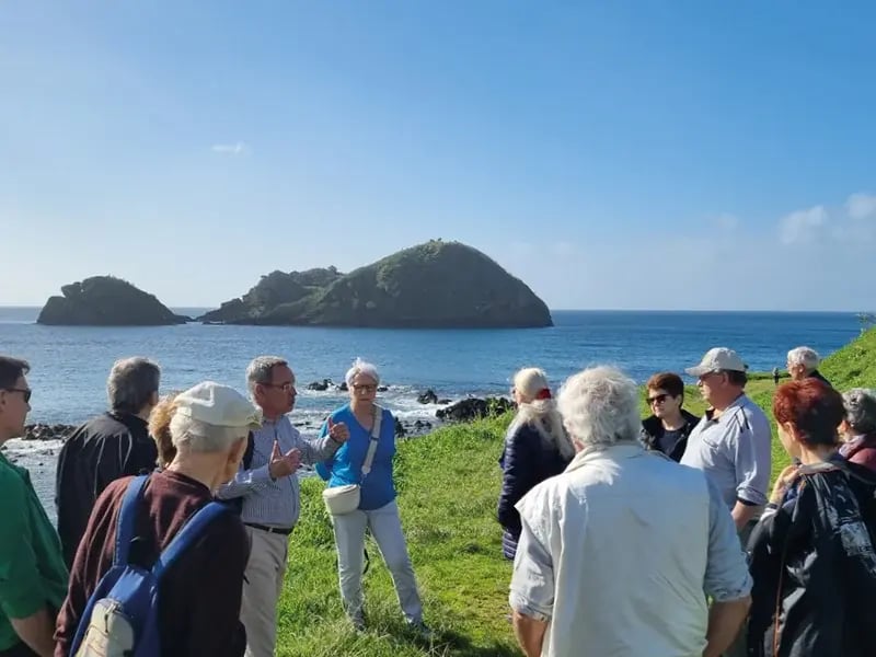Gruppe von älteren Menschen steht an einer Küste und blickt auf das Meer mit kleinen Inseln