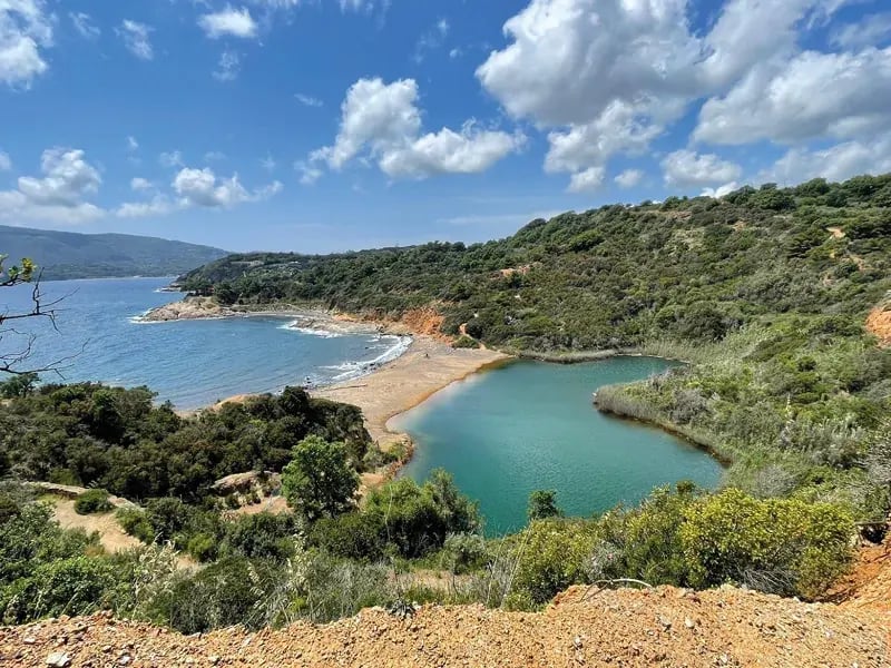 Küstenlandschaft mit Bucht, grüner Vegetation und blauem Wasser unter wolkigem Himmel