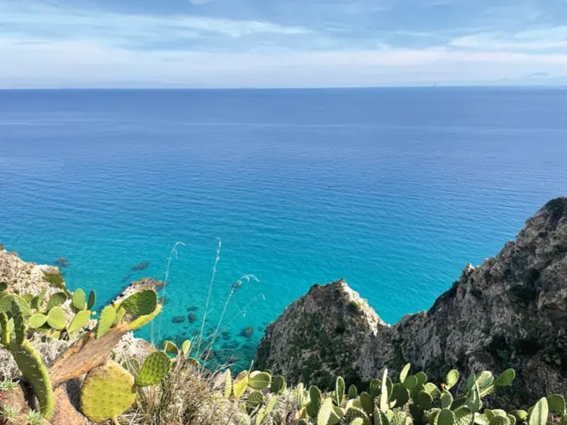 Blick von felsiger Küste mit Kakteen auf türkisfarbenes Meer und weiten Horizont