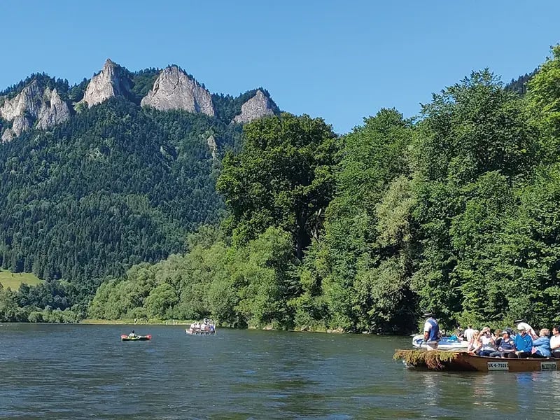 Flusslandschaft mit bewaldeten Bergen, Felsen und Booten auf dem Wasser