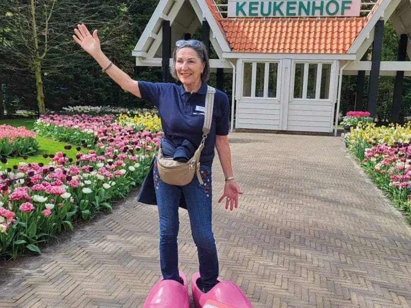 Reiseleiterin steht auf grossen Holzschuhen vor Eingang mit Schriftzug Keukenhof und Blumenbeeten