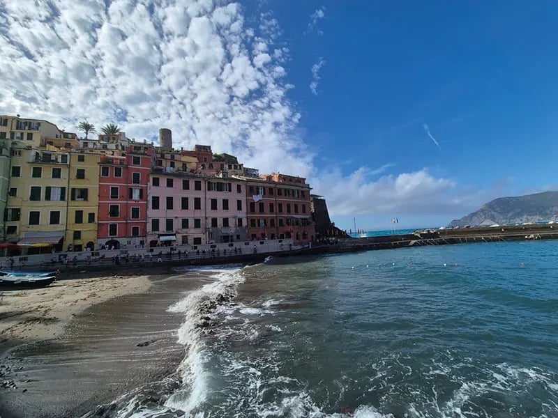 Küstenort mit bunten Häusern am Strand, Wellen am Ufer und blauem Himmel mit Wolken