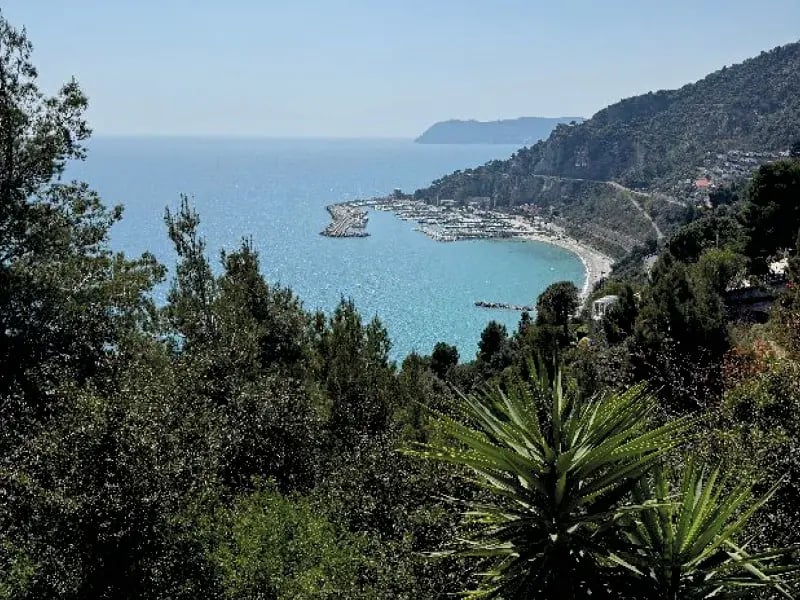 Küstenbucht mit Hafen, blauem Meer und bewaldeten Hügeln im Hintergrund