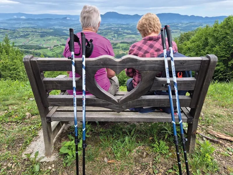 Zwei Personen sitzen auf einer Bank mit Herzform und blicken auf eine grüne Landschaft
