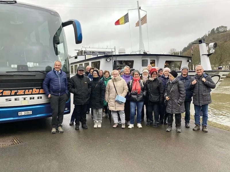 Gruppe von Menschen steht neben einem Reisebus und einem Schiff an einem Flussufer
