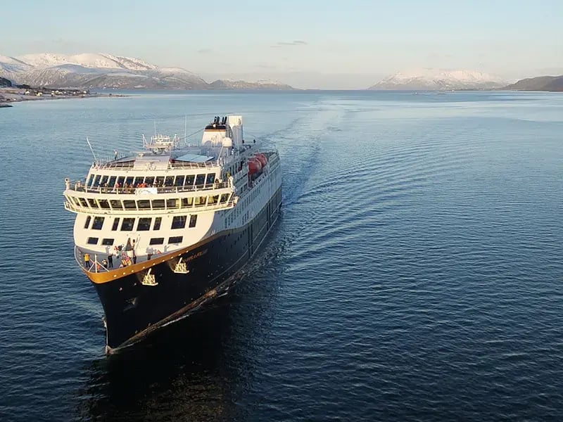 Kreuzfahrtschiff fährt auf ruhigem Meer mit schneebedeckten Bergen im Hintergrund