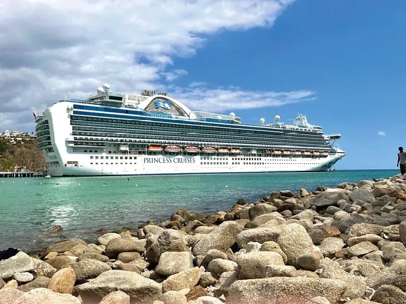 Grosses Kreuzfahrtschiff liegt nahe der Küste vor türkisfarbenem Meer und steinigem Ufer