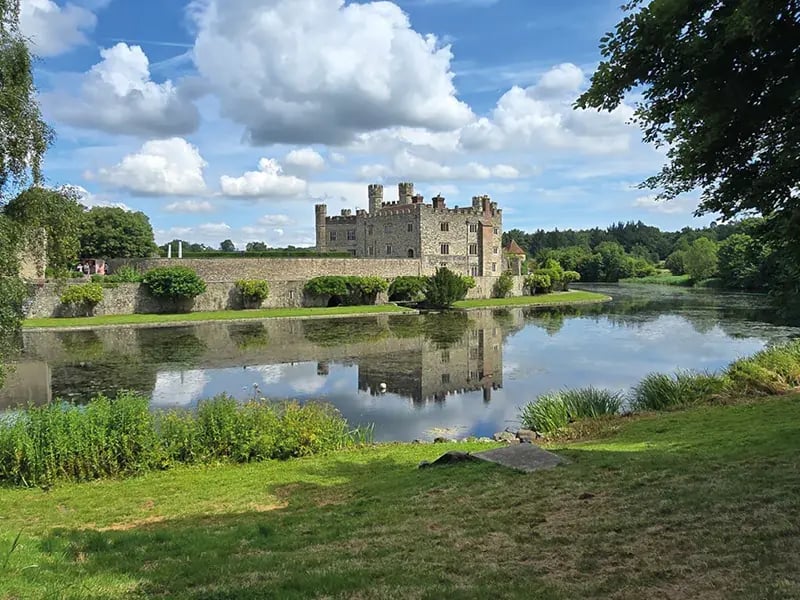 Schloss am Fluss mit Spiegelung im Wasser und grünem Ufer