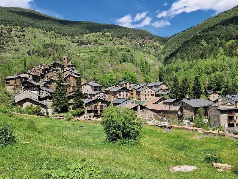 Bergdorf mit Steinhäusern in grüner Landschaft und bewaldeten Hängen