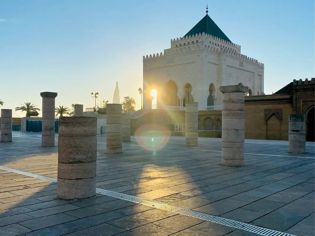 Historisches Mausoleum mit grünem Dach und Säulen im Vordergrund, Sonne tief am Himmel
