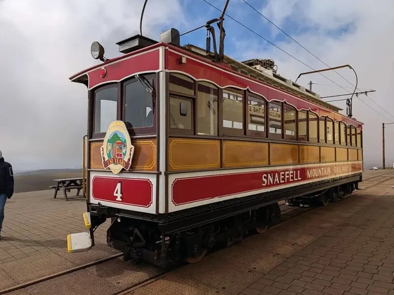 Un wagon historique rouge et crème de la Snaefell Mountain Railway, portant le numéro 4, stationné au sommet d'une montagne sous un ciel nuageux.