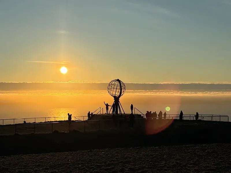 Sonnenuntergang am Meer mit Menschen und Weltkugel Skulptur auf einer Plattform