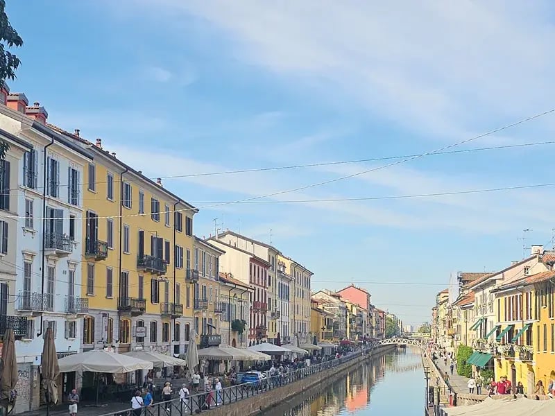 Kanal mit Uferpromenade und bunten Häusern, Menschen spazieren entlang des Wassers