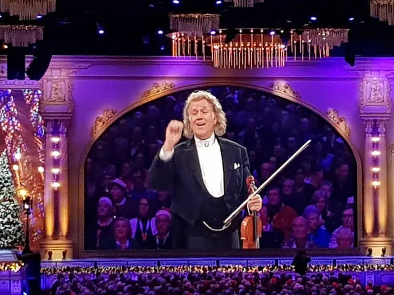 Dirigent im Konzertsaal steht vor Orchester und Publikum, festlich beleuchtete Bühne im Hintergrund