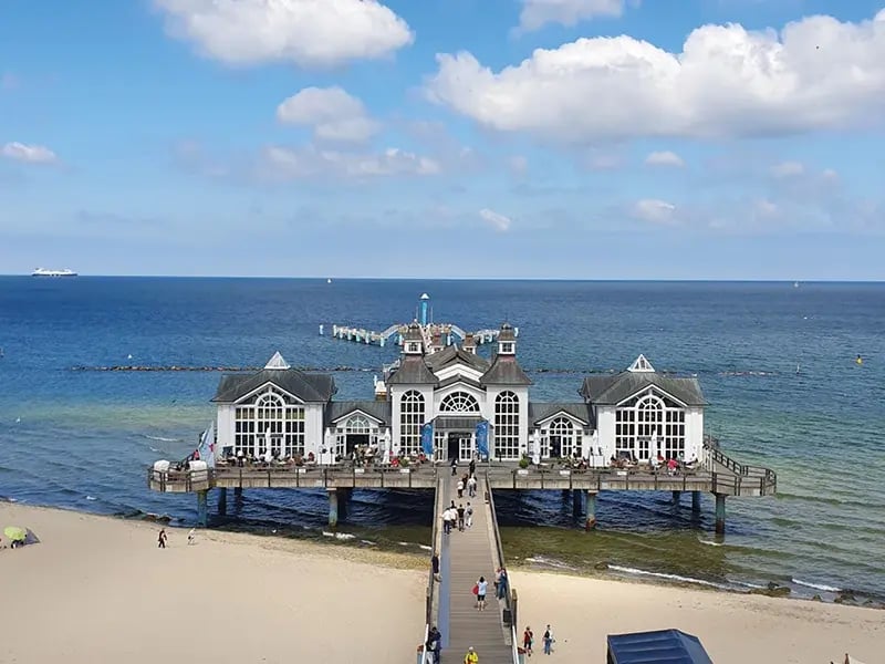 Seebrücke mit Gebäude im Meer, Strand und blauem Himmel mit Wolken